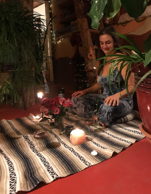 Lisa Marie seated on a woven blanket surrounded by candles, roses, and plants during a ceremony
